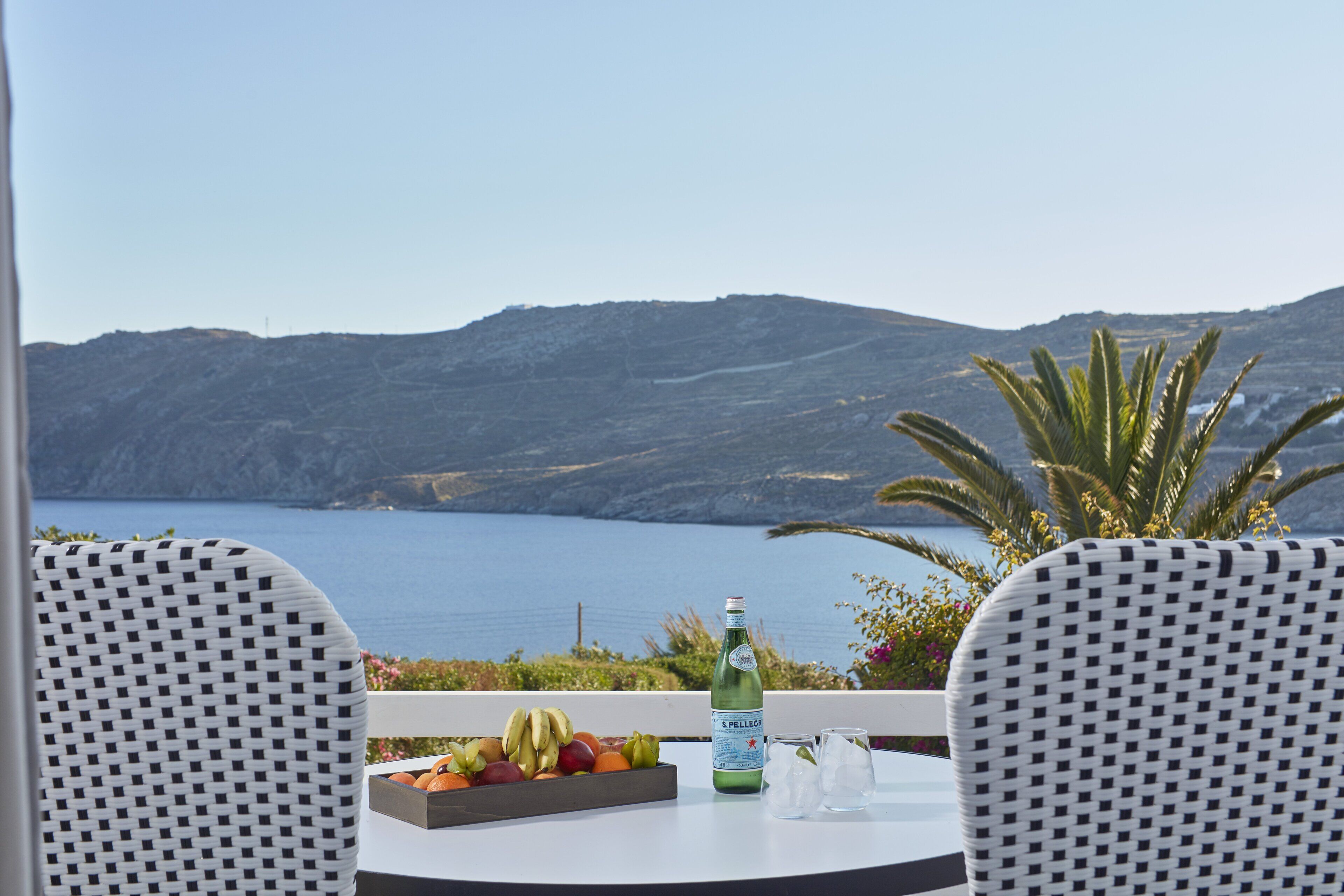 A table with a bottle of S. Pellegrino water, ice cubes, and a fruit tray on a balcony overlooking a body of water and hills.