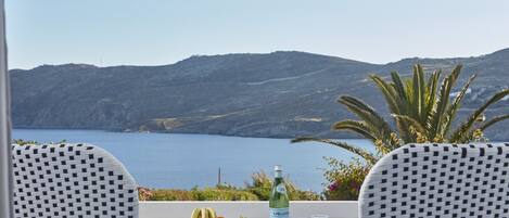 A table with a bottle of S. Pellegrino water, ice cubes, and a fruit tray on a balcony overlooking a body of water and hills.