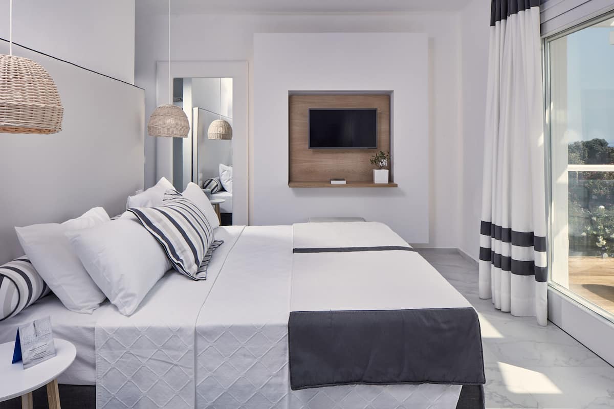 Habitación de hotel moderna con una cama grande, televisor montado y vistas al balcón.
