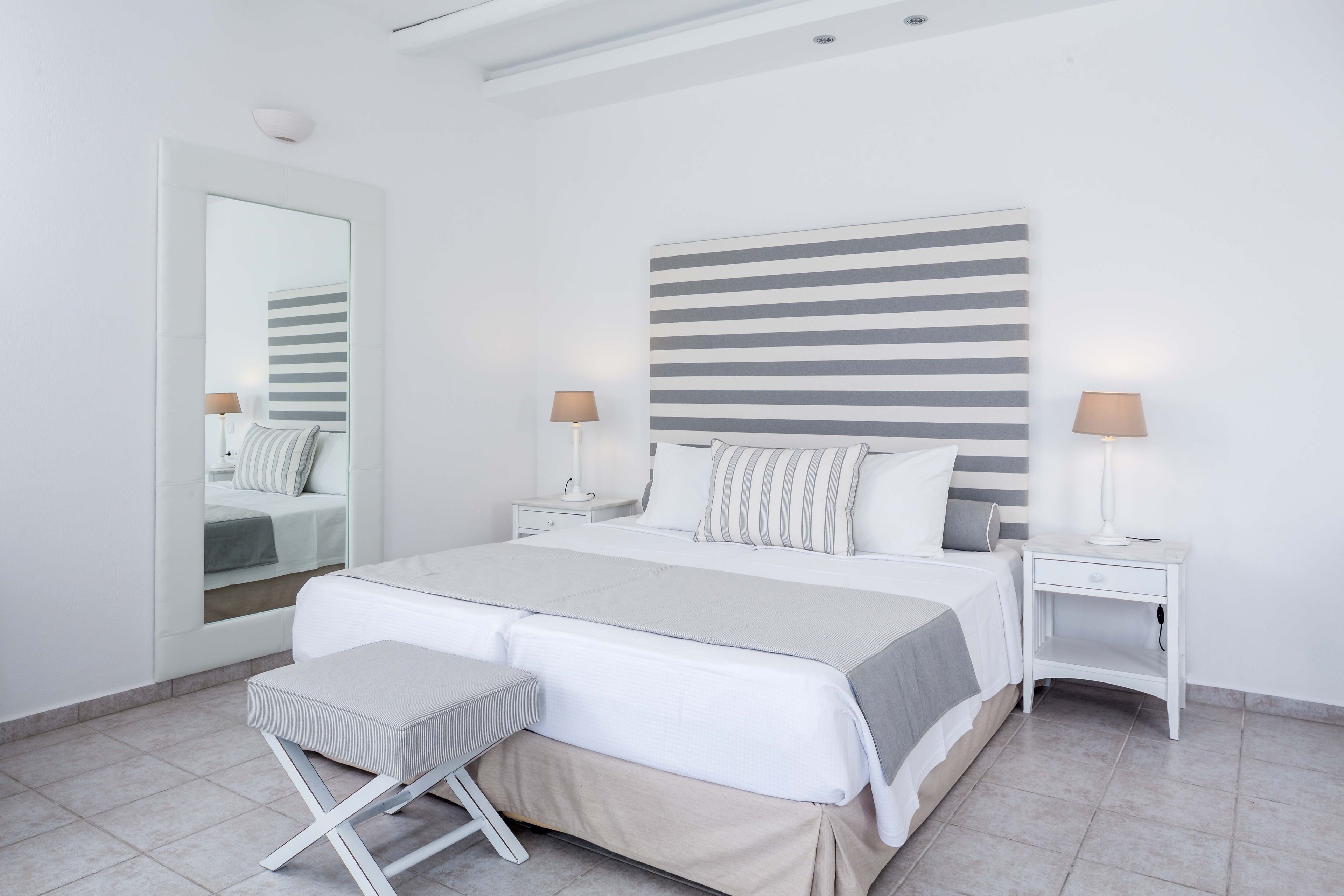A modern bedroom with a large bed, bedside tables, a mirror, and a bench.
