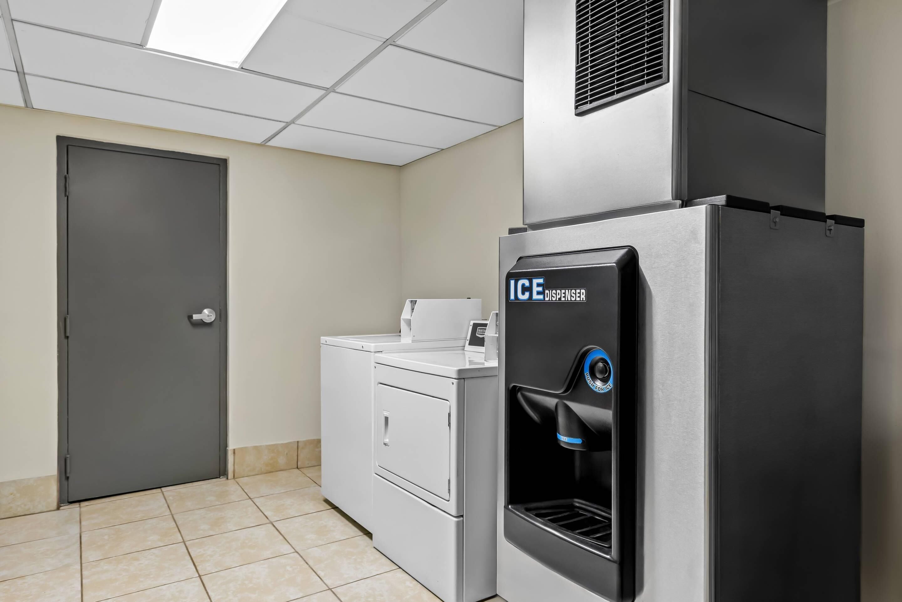 A laundry room with a gray door, a white washing machine, and a black ice dispenser.