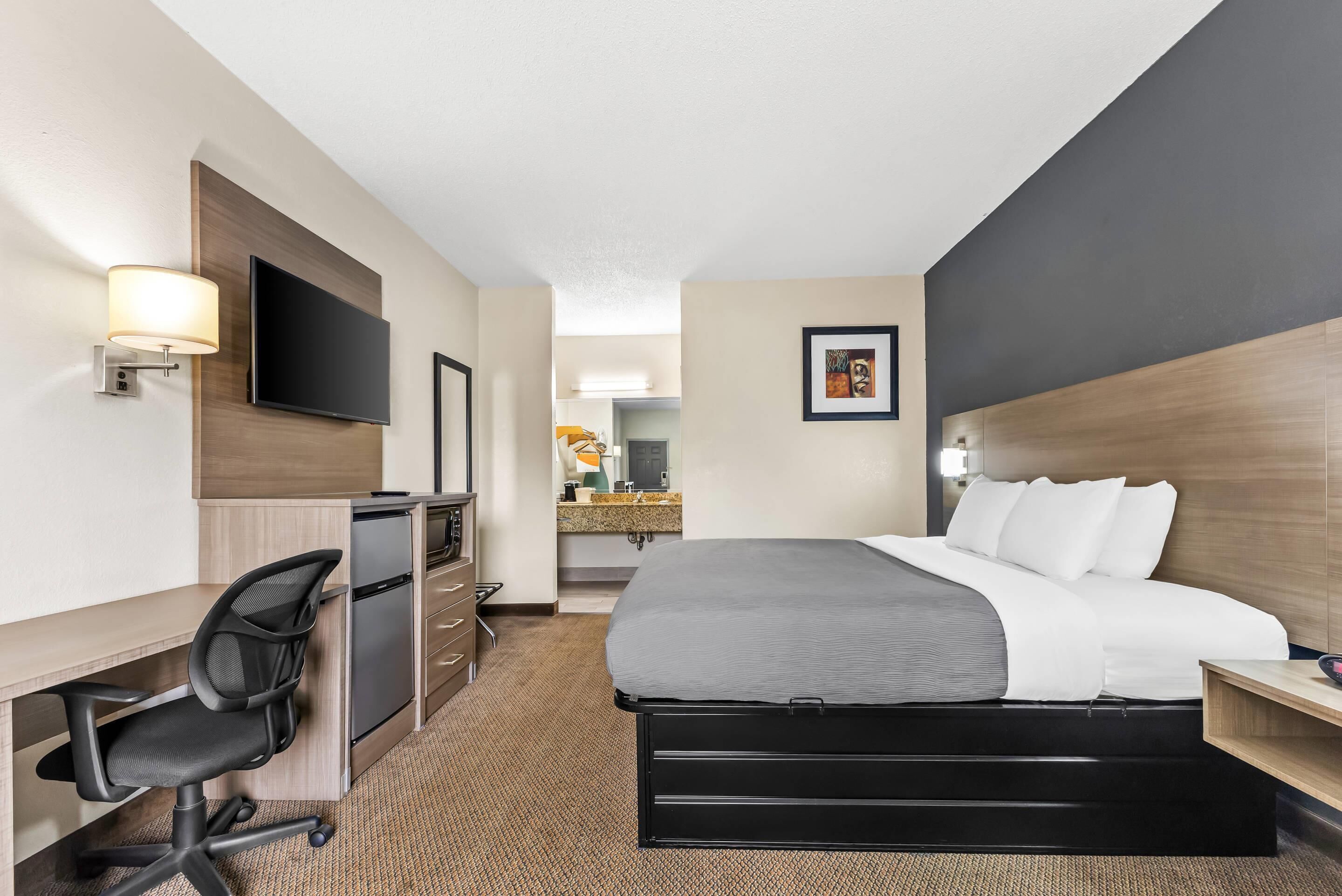 A hotel room with a bed, desk, chair, TV, and a bathroom visible in the background.