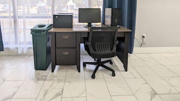 Un espacio de trabajo con una computadora de escritorio, un monitor e impresora sobre un escritorio, un cubo de basura y una silla.
