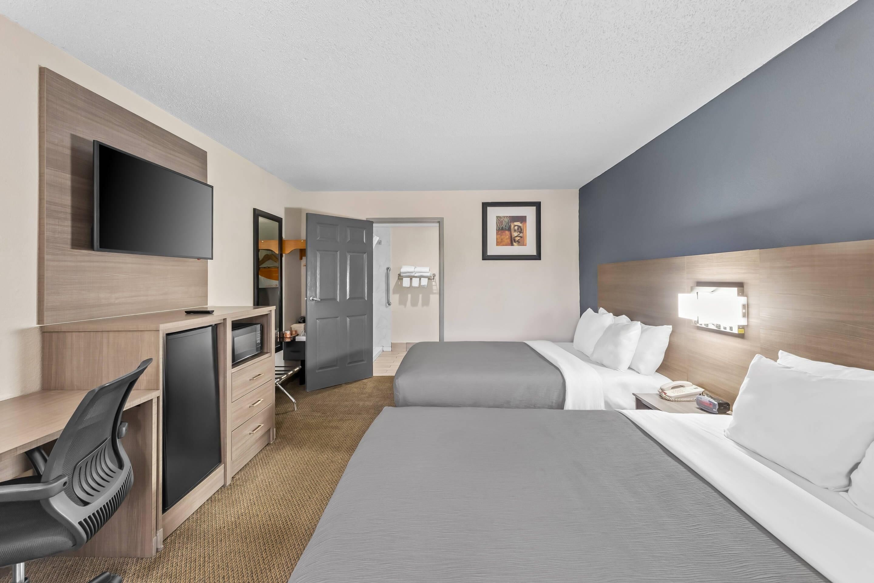 A hotel room with a bed, desk, chair, TV, and a door leading to a bathroom.