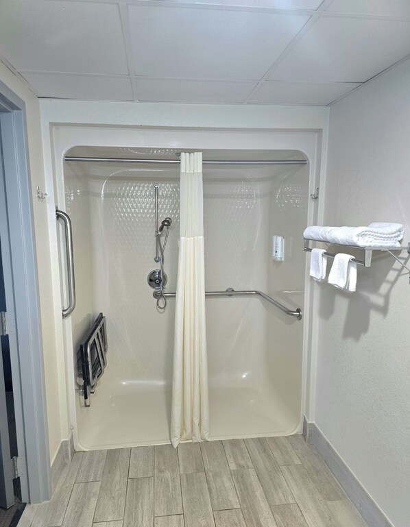 Ducha accesible en silla de ruedas con puerta de vidrio, un perchero con toallas y una barra de apoyo.