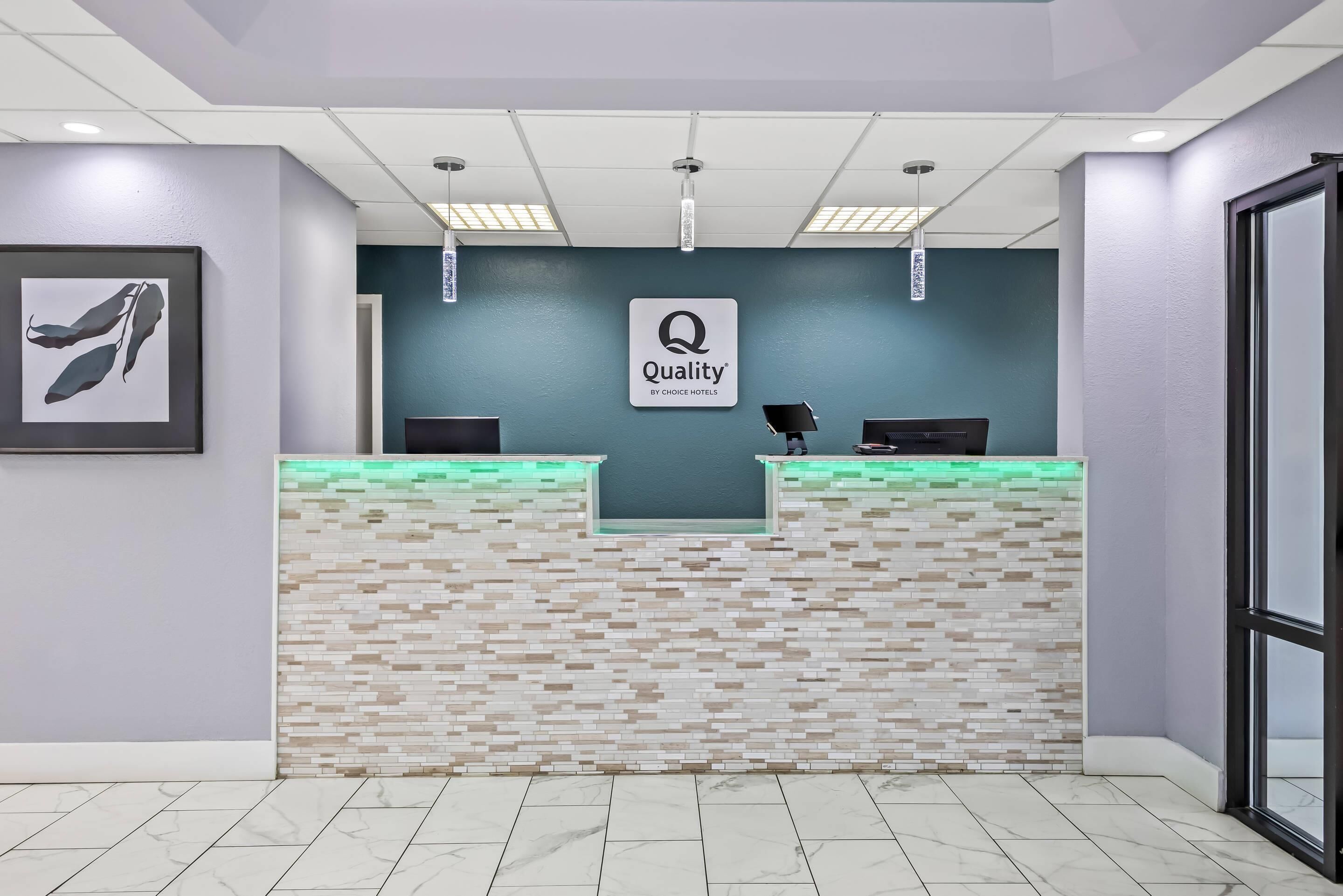 Un mostrador de recepción con un cartel de 'Quality by Choice Hotels', suelo de baldosas y una obra de arte enmarcada en la pared.