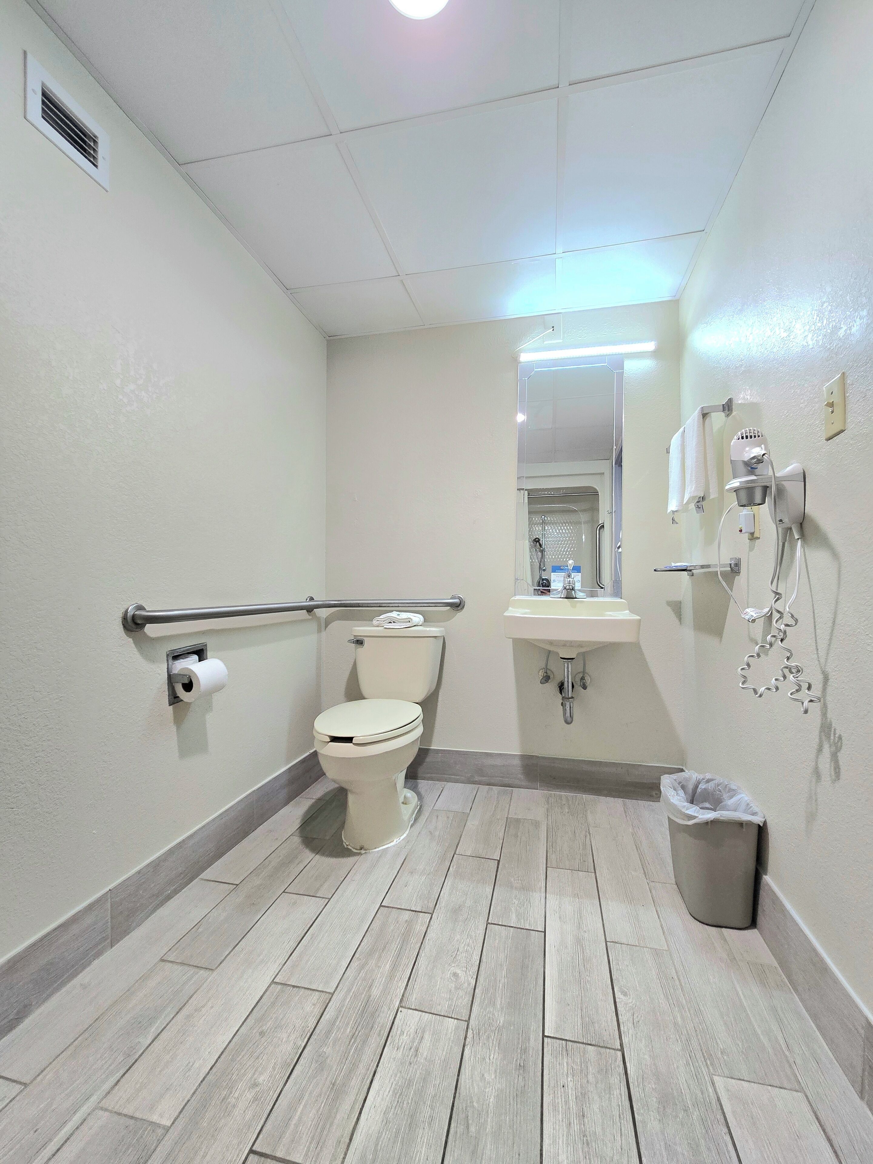 A bathroom with a toilet, a hand dryer, a sink, and a trash can.