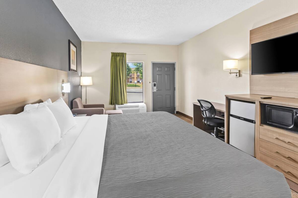 A hotel room with a large bed, a desk with a computer, a TV, and a microwave.