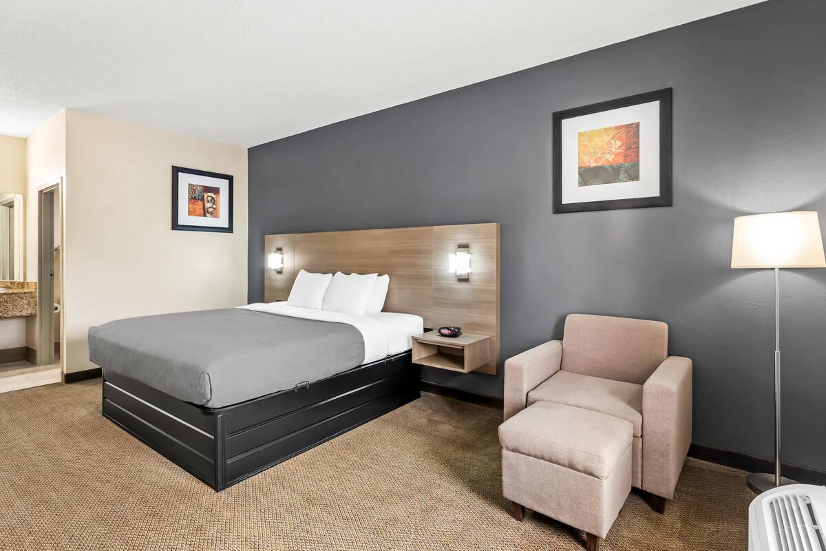 A hotel room with a bed, a chair, a nightstand, and two wall-mounted lamps.