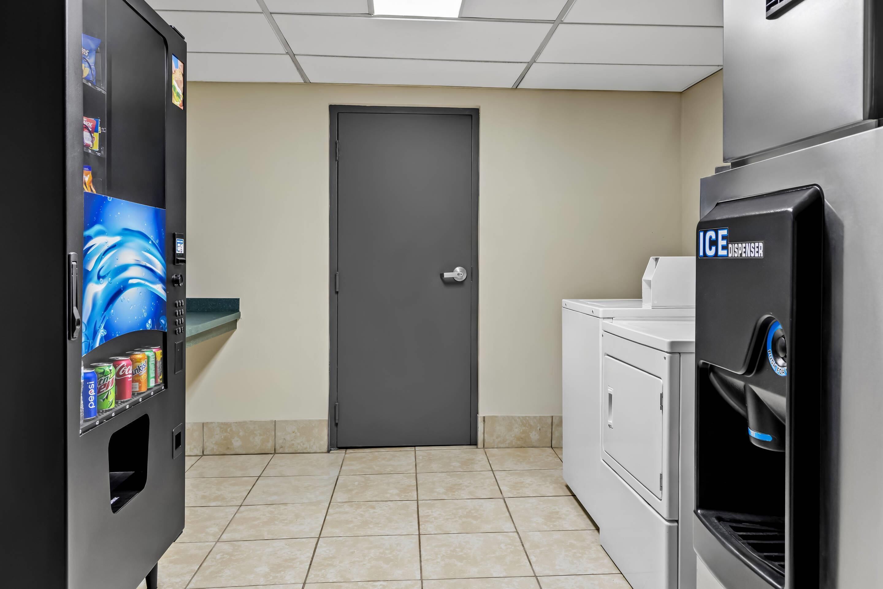 A kitchenette with a refrigerator, an ice dispenser, and a vending machine with beverages.