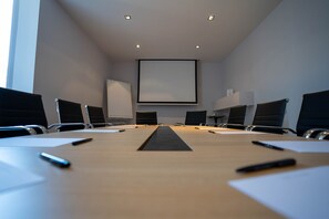 Conference room with a long table and six chairs, featuring a large projection screen at the front.
