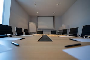 Conference room with a long table and six chairs, featuring a large projection screen at the front.