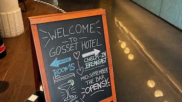 Señal de bienvenida en el Hotel Gosset con flechas indicando la dirección a servicios como habitaciones, desayuno y el bar.