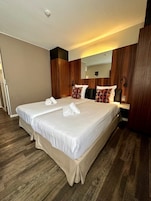 Una habitación de hotel con una cama grande, dos mesitas de noche, un espejo y suelo de madera.