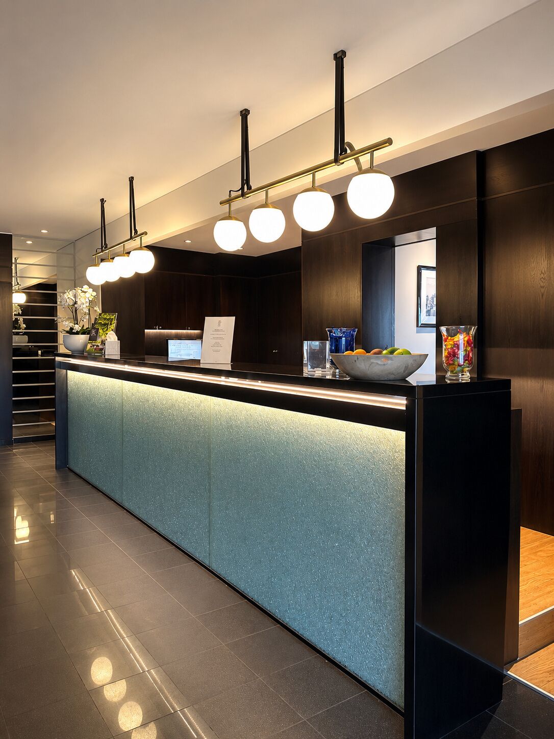 A modern reception desk with a glass top, overhead lighting, and a digital display.