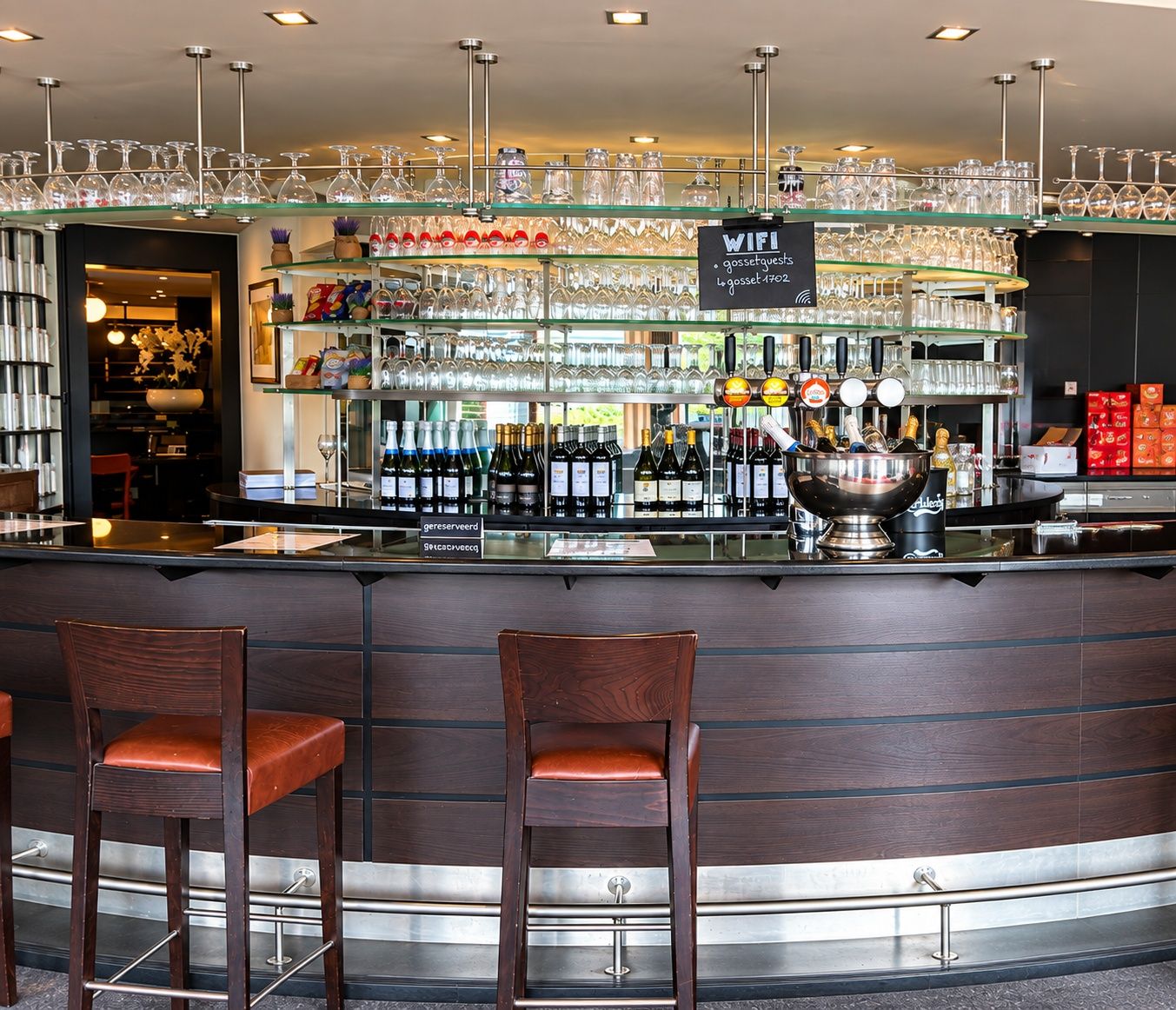 Zona de bar con mostrador, taburetes y una variedad de copas y botellas.