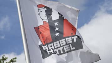 Una bandera con un logotipo y el texto "KASSE HOTEL" en un asta, frente a un cielo nublado.