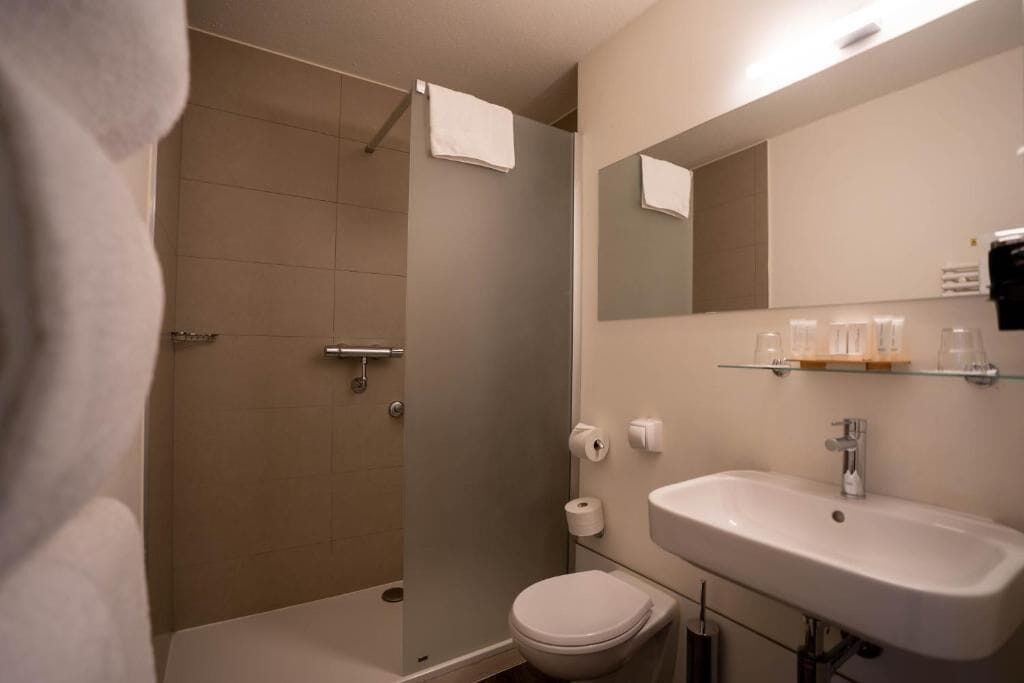 A bathroom with a shower, toilet, sink, and mirror.
