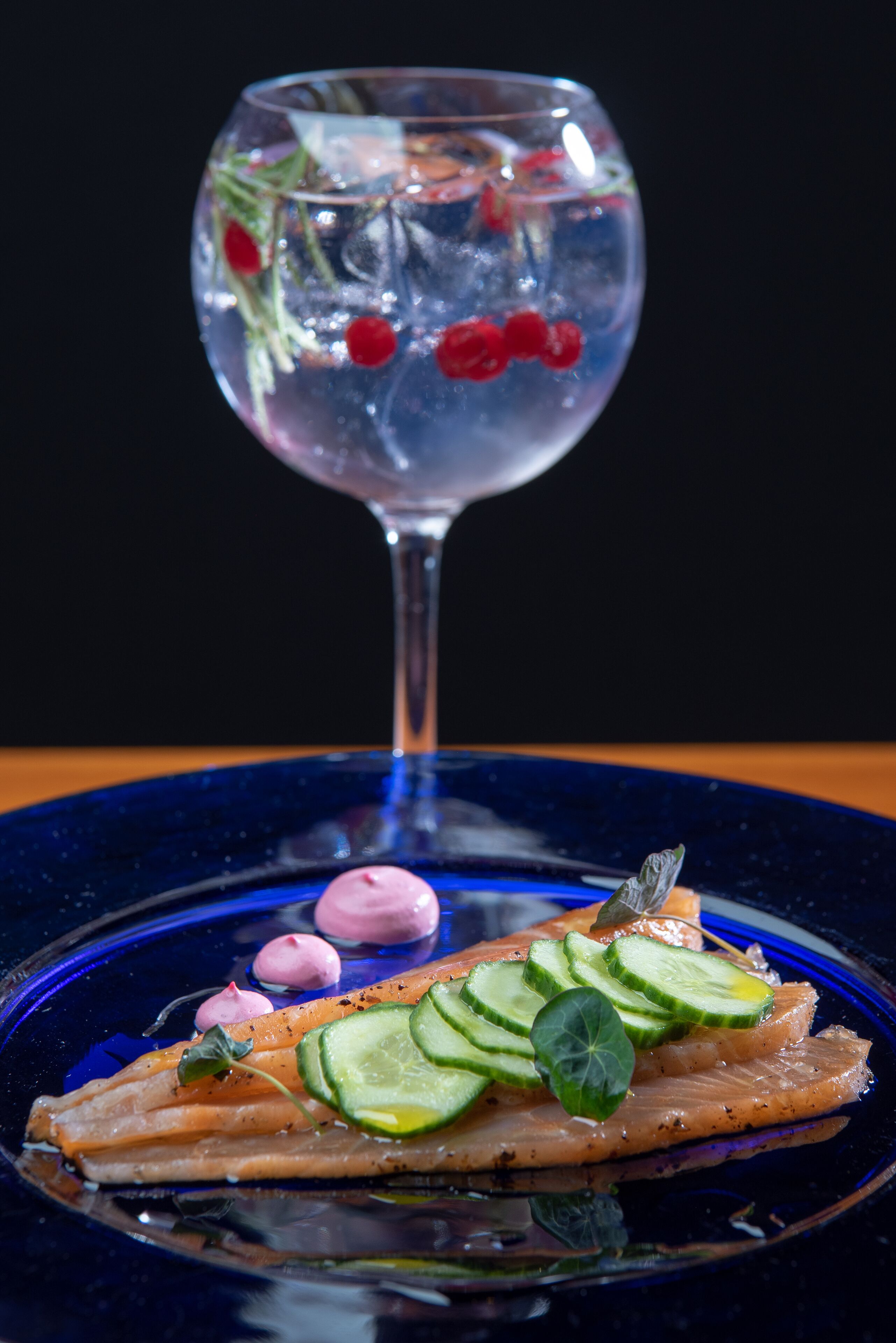 A blue plate with salmon, cucumber slices, and a glass of water with berries.