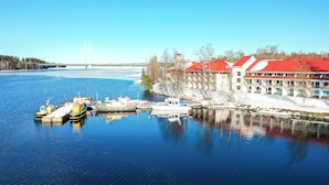 A waterfront hotel with a red roof, docked boats, and a bridge in the background. - Kumpeli Spa (Heinola)