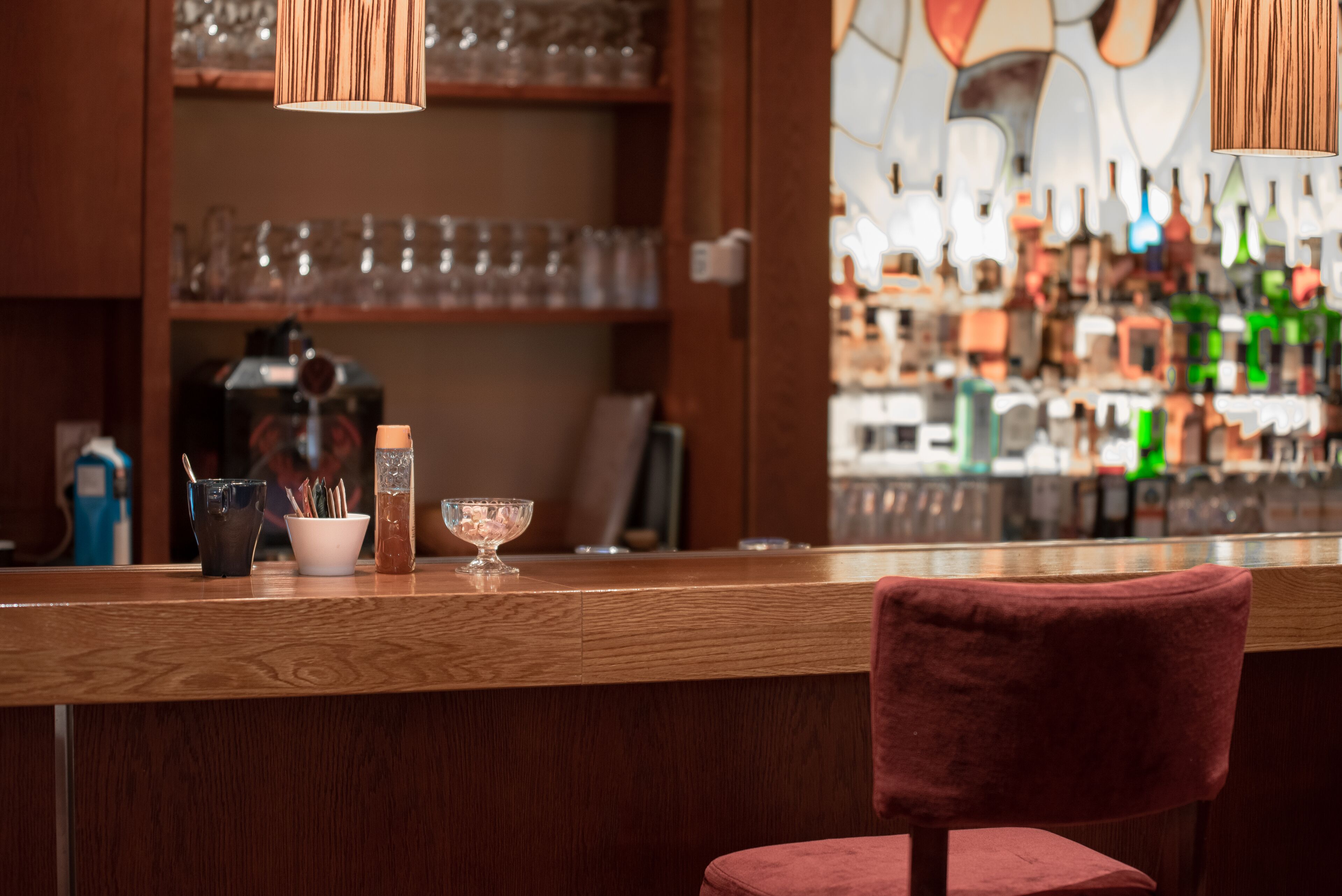 A bar area with a wooden counter, a red chair, and shelves with glassware.