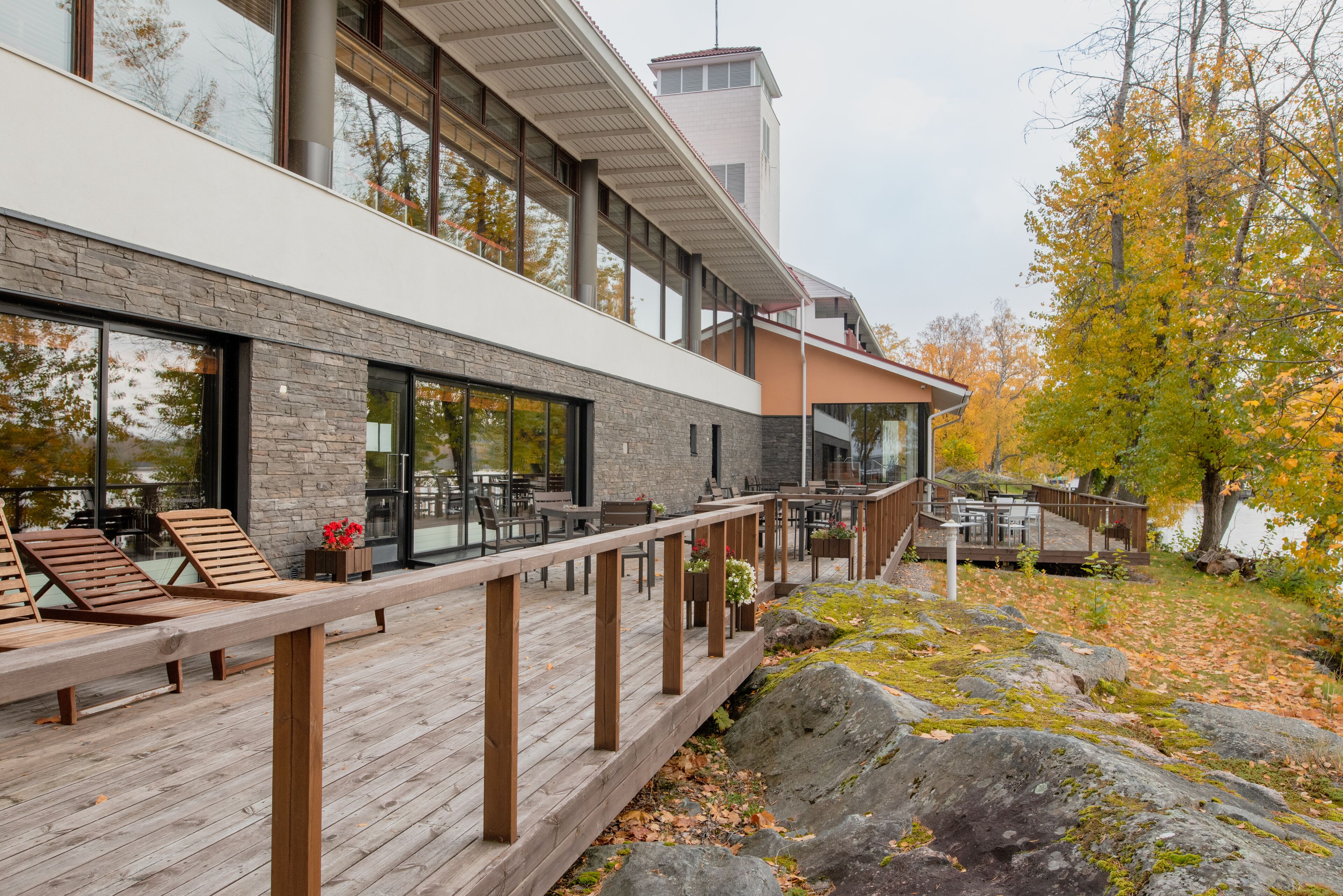 A modern building with a wooden deck, large windows, and outdoor seating.