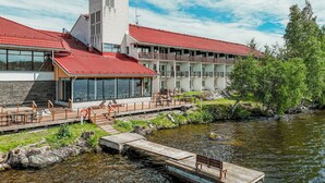 A hotel with a red-tiled roof, a tower, and a dock extending into a river. - Kumpeli Spa (Heinola)