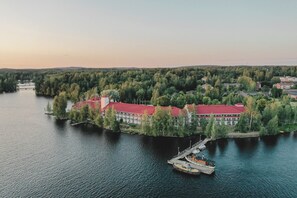 Vista aérea de un hotel a orillas del lago, con un edificio de techo rojo, barcos amarrados y una zona boscosa circundante.