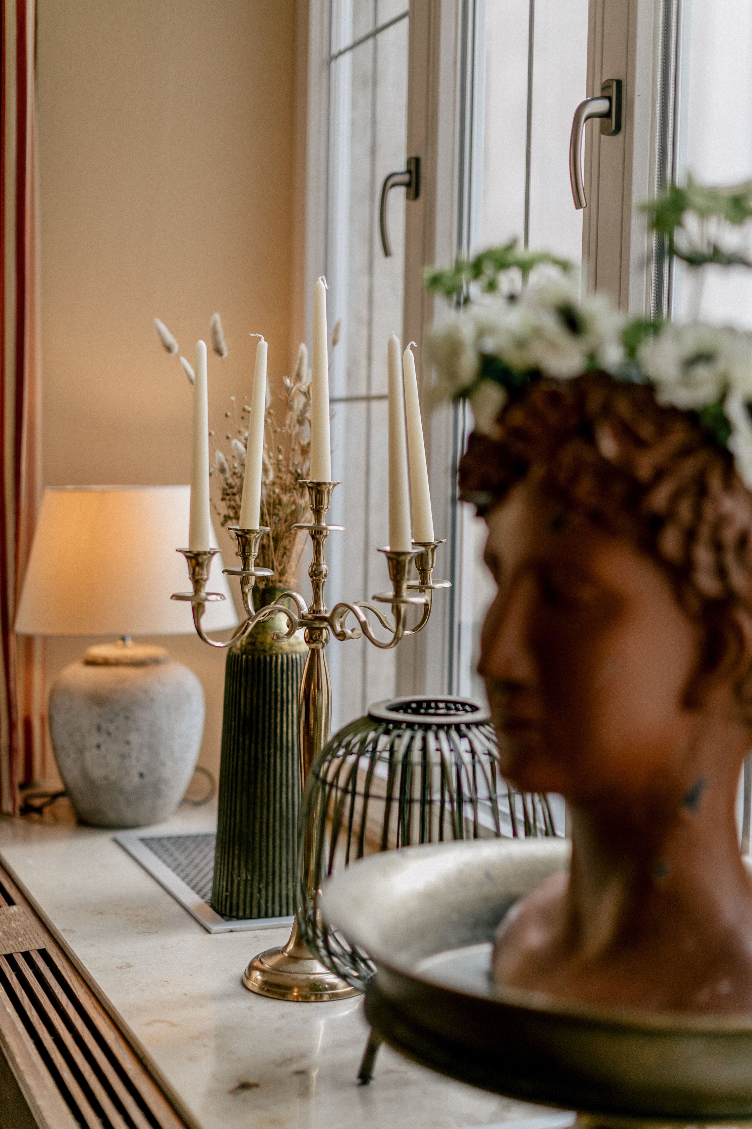 A decorative candelabra with candles, a vase with dried flowers, and a ceramic bust on a marble surface.