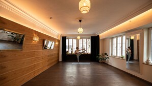 Ein geräumiger Raum mit Holzvertäfelung, großen Fenstern und einem Spiegel, der eine sich streckende Person widerspiegelt.