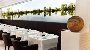 A restaurant with tables set for dining, a large vase on display, and a mural of a lake with trees. - Boutique Villa am Ruhrufer Retreat (Muelheim an der Ruhr)