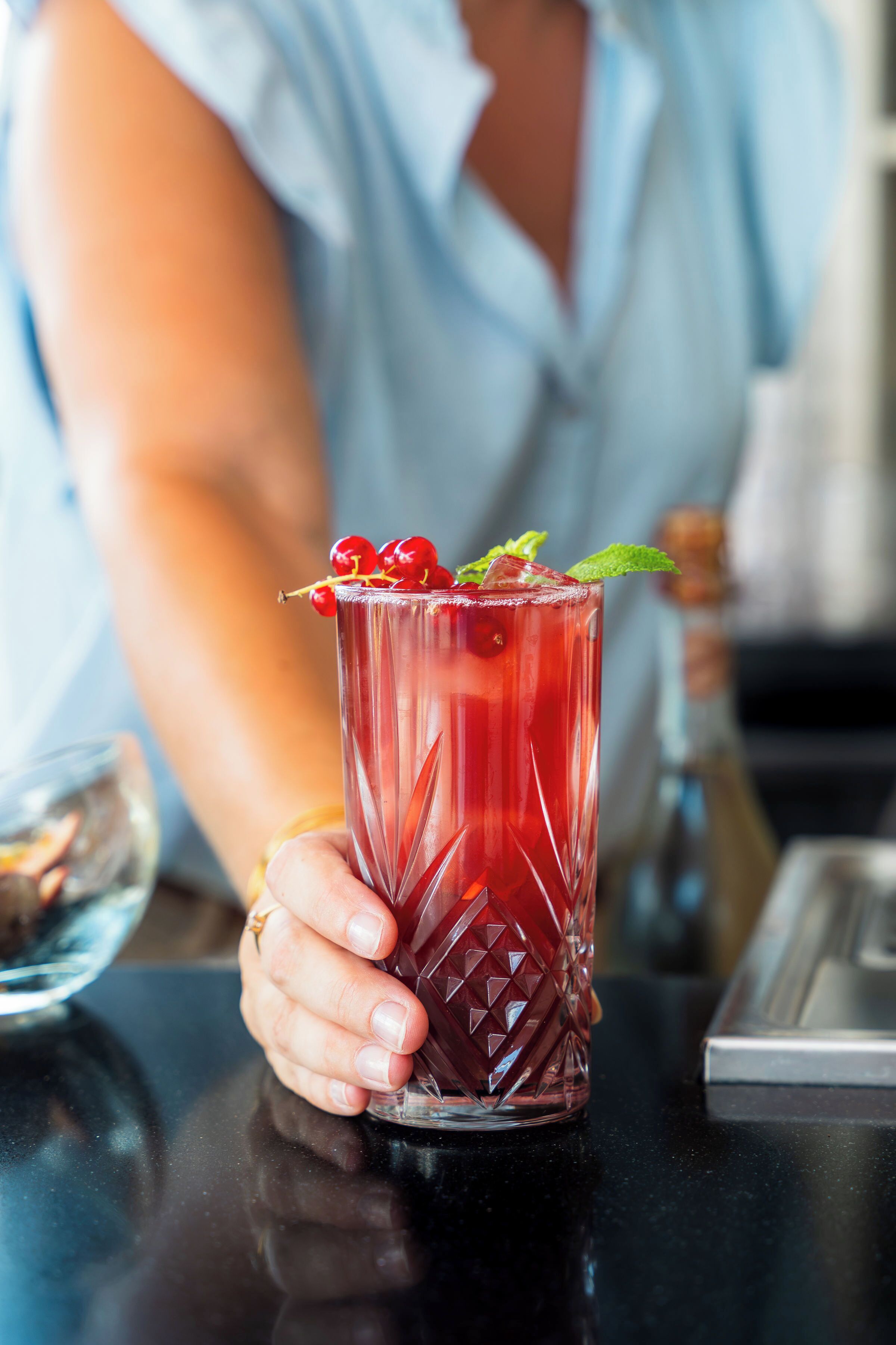 Iemand houdt een glas met een rood drankje vast, versierd met bessen en munt.