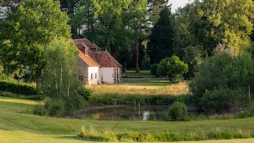 Una casa rustica con tetto in tegole, immersa nel verde e con un piccolo stagno.