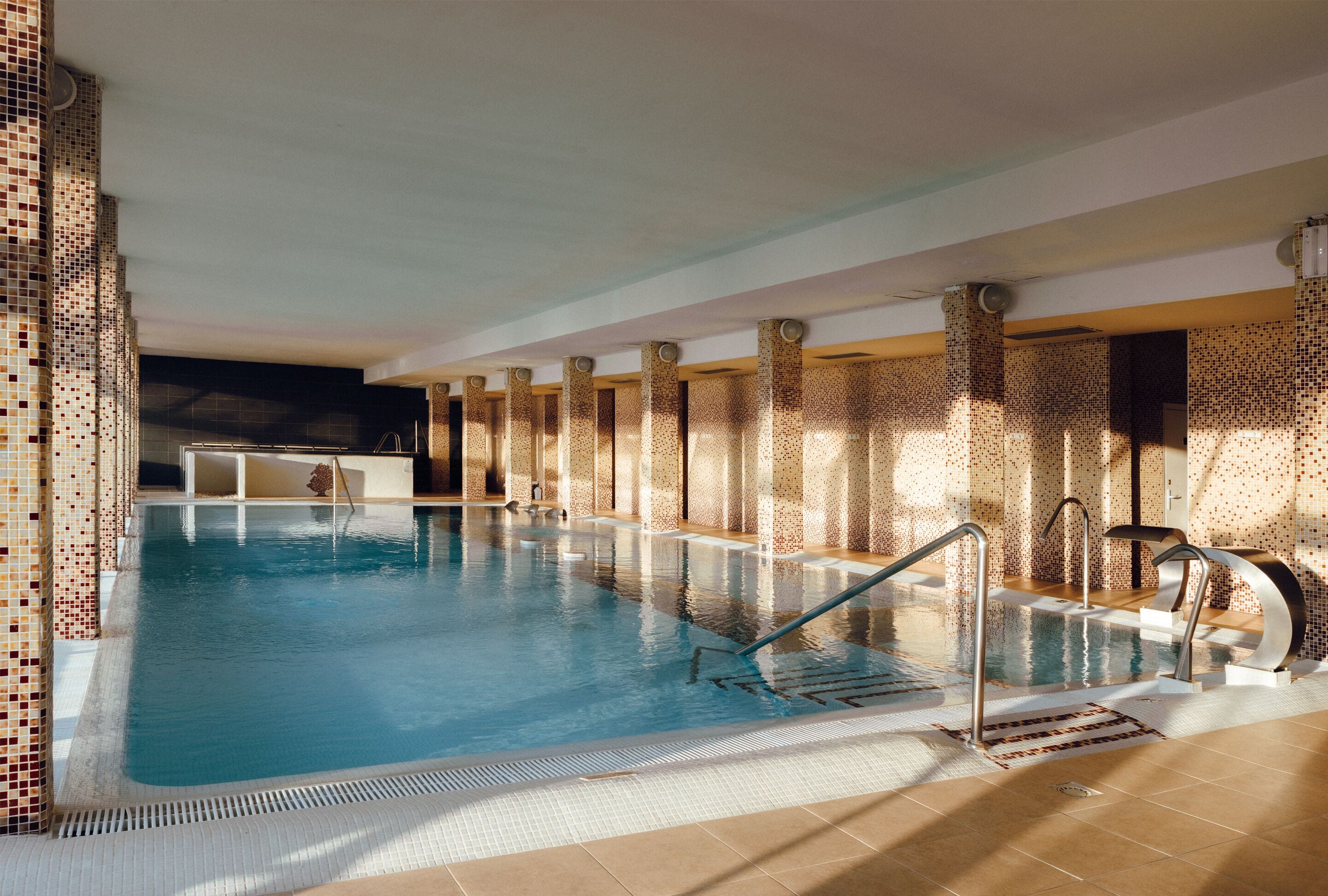 Una piscina interior con paredes de azulejos y zona acuática transparente.