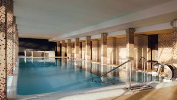 Una piscina interior con paredes de azulejos y zona acuática transparente.