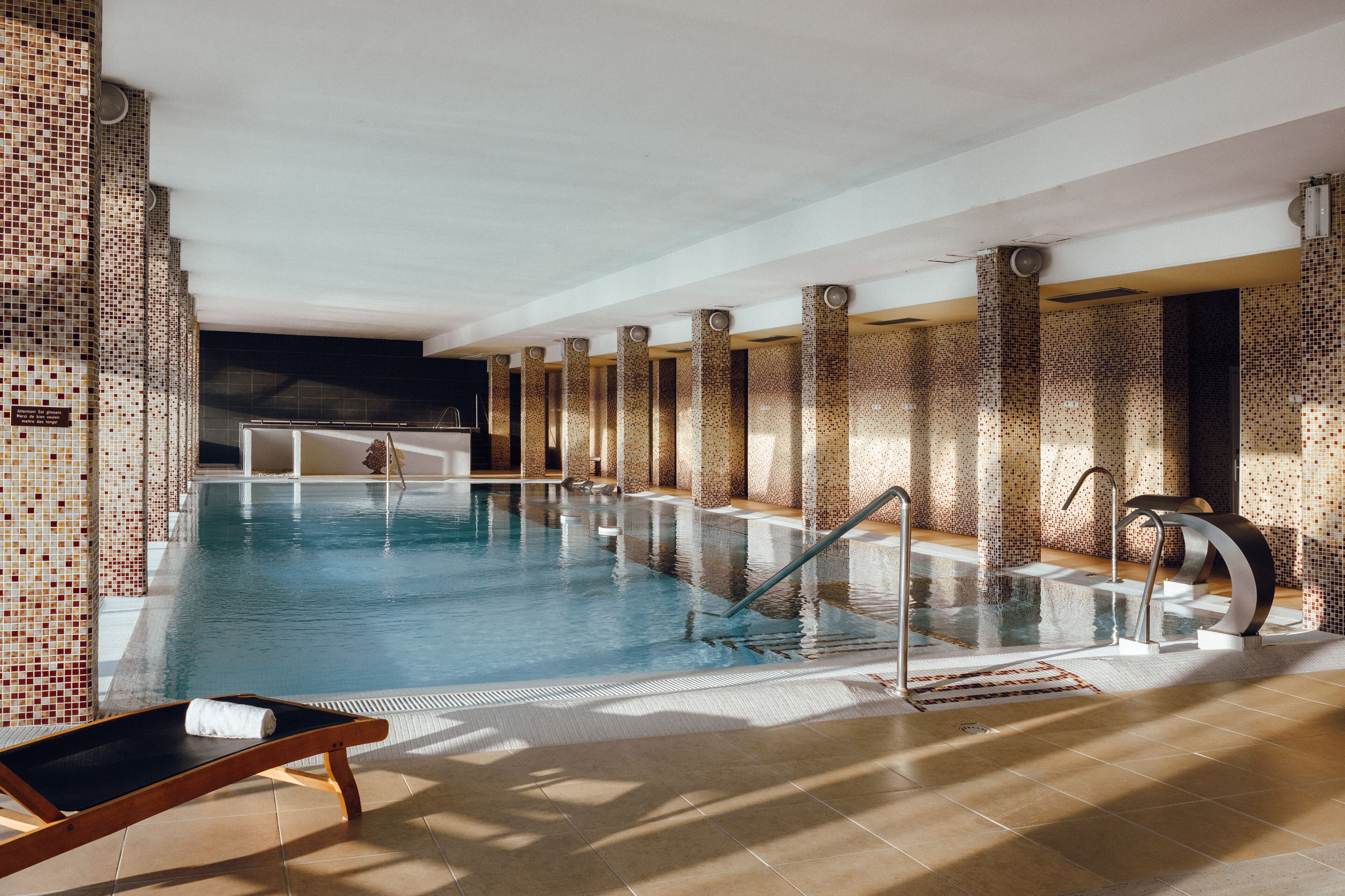 A swimming pool with tiled walls and columns, a lounge chair, and a sunshade.