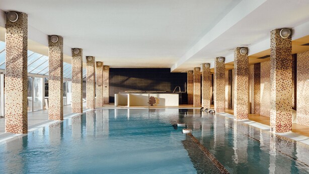 An indoor swimming pool with tiled columns and a clear blue water surface.