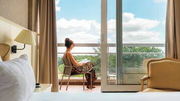Une pièce comprenant un lit, une chaise, une table et une fenêtre donnant sur des arbres et le ciel.