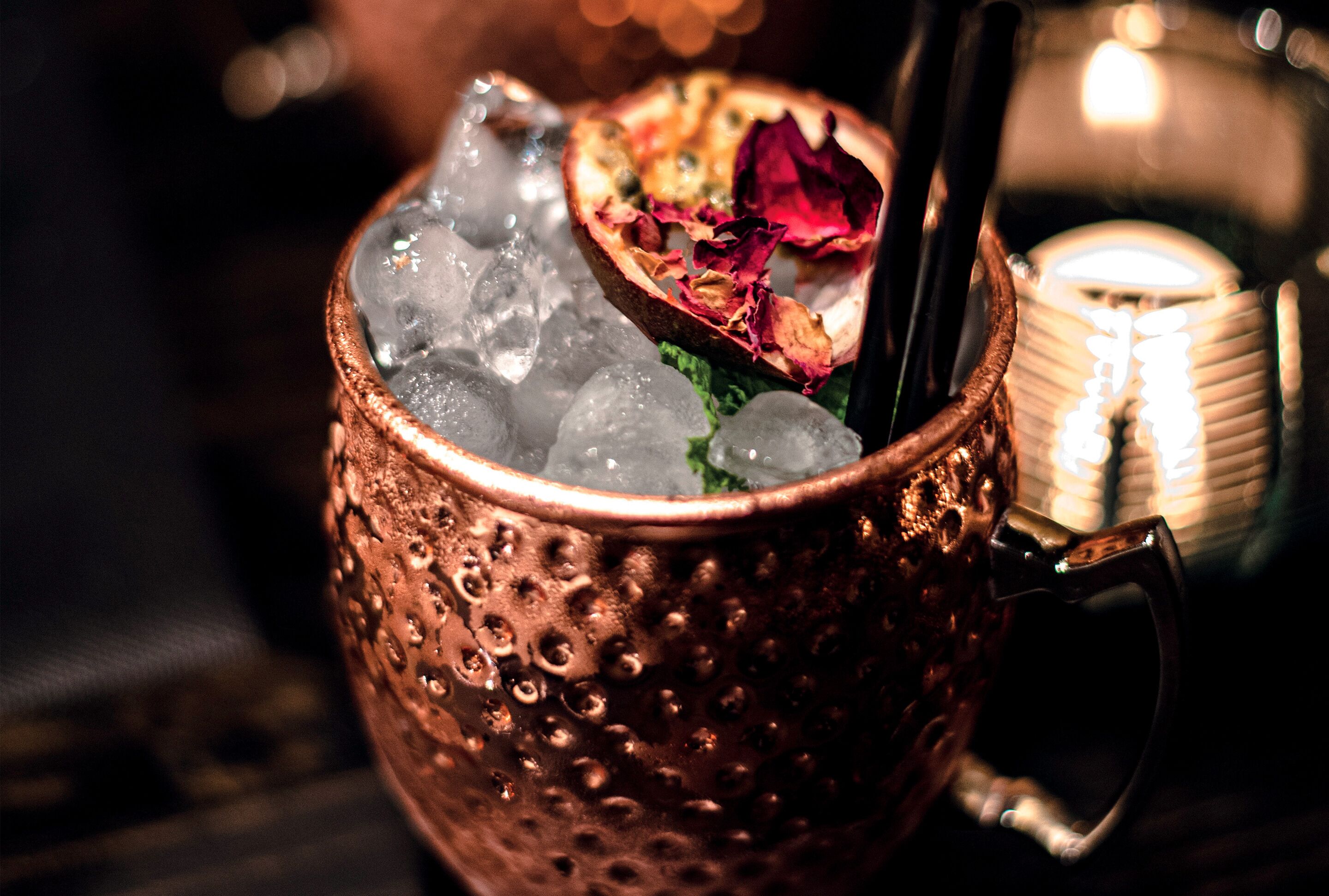 Una taza de cobre llena de hielo y una bebida, adornada con pétalos de rosa.