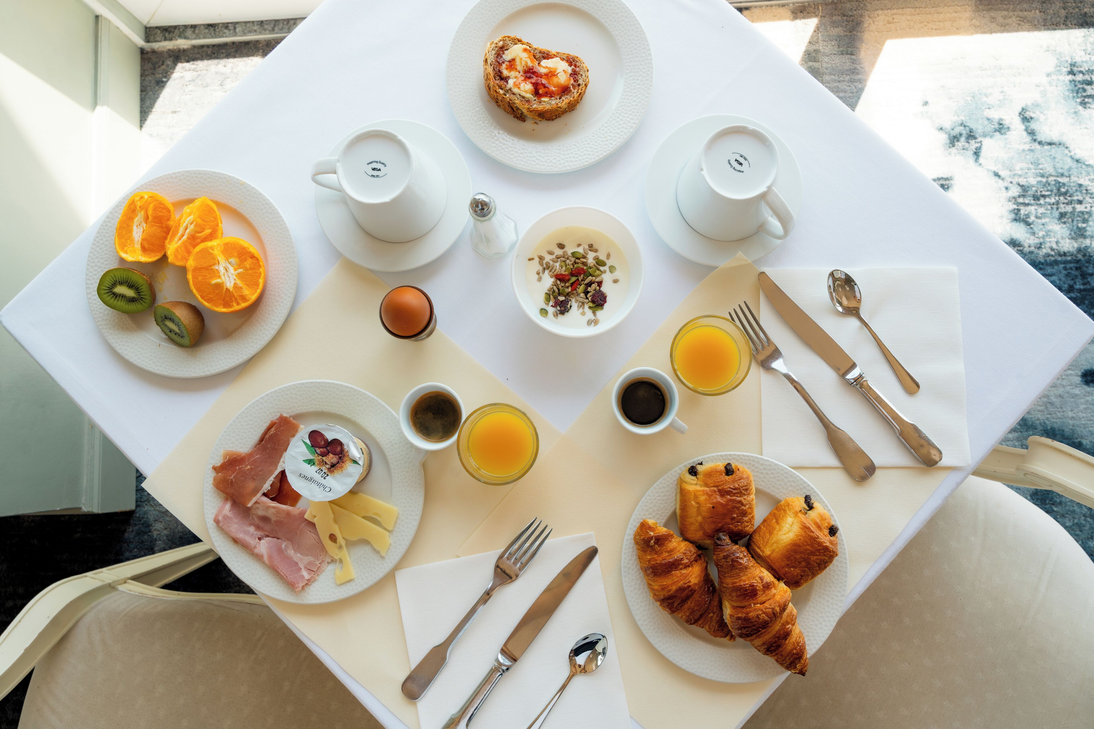 Una mesa de desayuno con platos de comida, cubiertos y tazas.