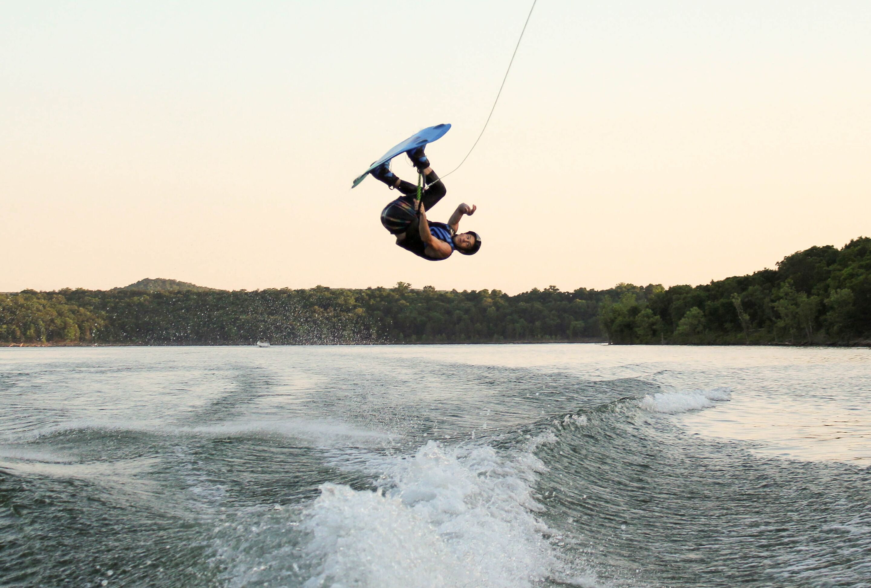 Eine Person wakeboardet auf einem See, im Hintergrund Bäume.