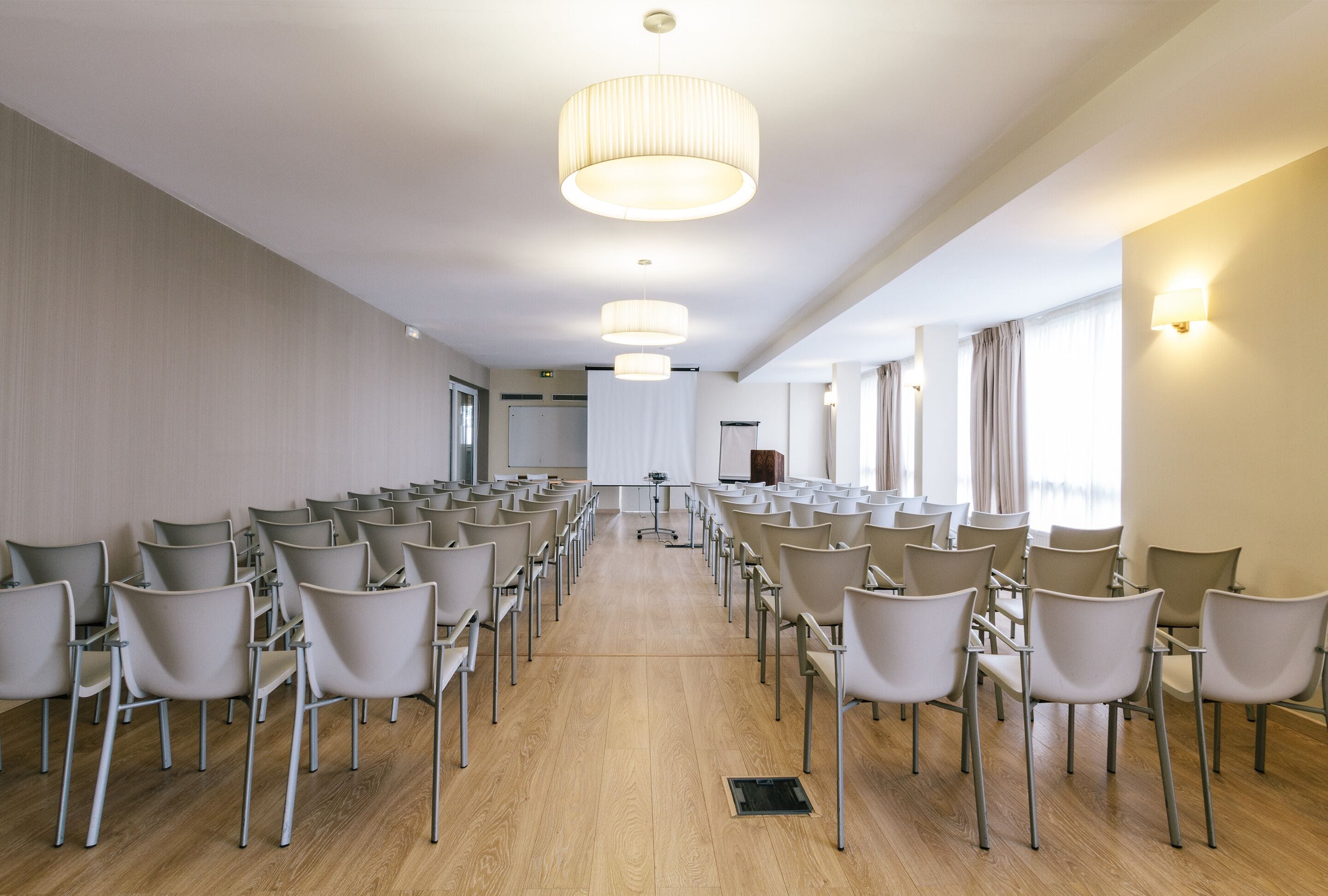 Un salón de conferencias con filas de sillas, un atril y un amplio ventanal con cortinas.