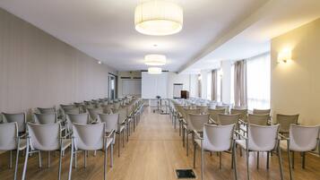Un salón de conferencias con filas de sillas, un atril y un amplio ventanal con cortinas.