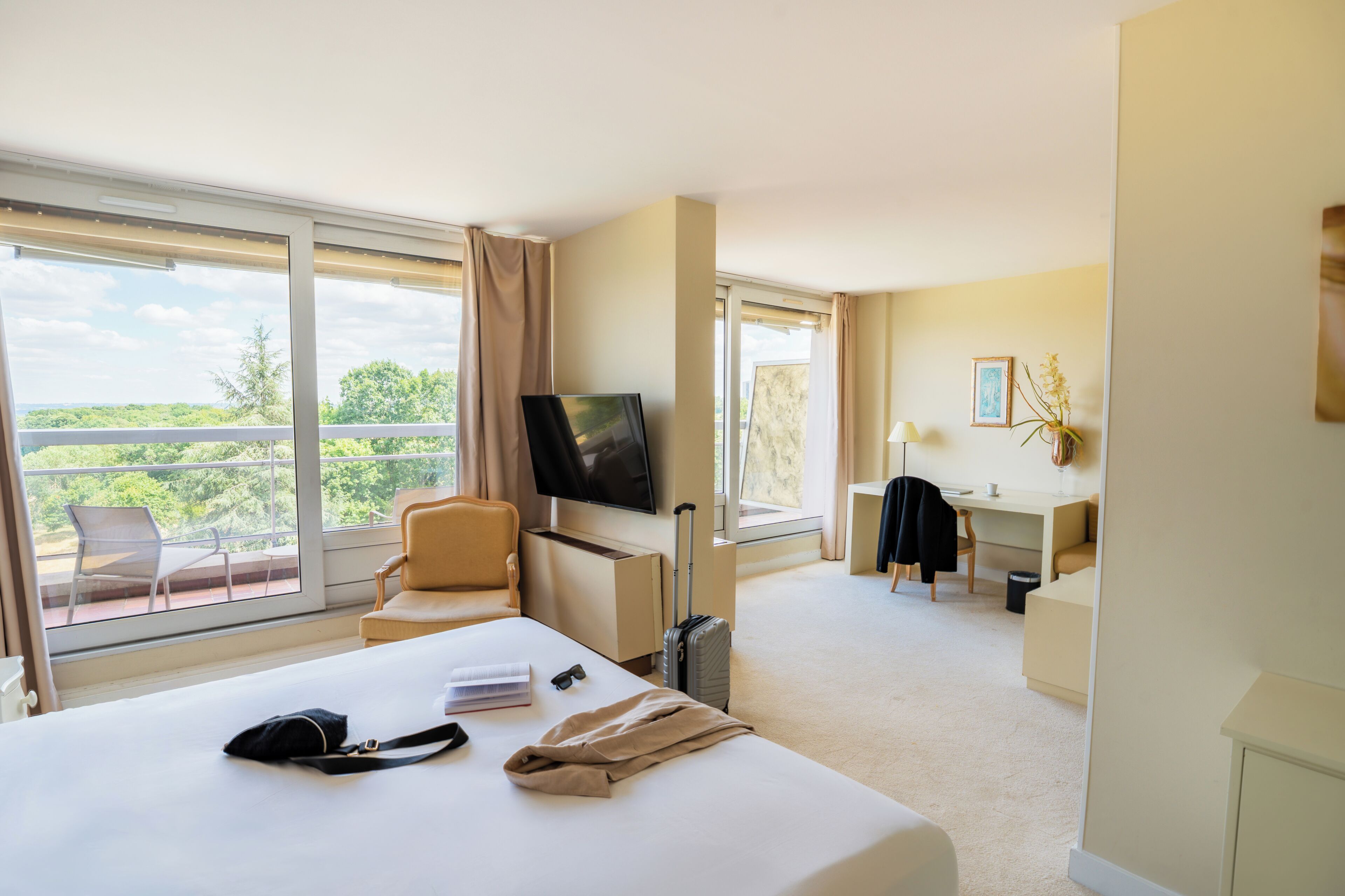Habitación de hotel con cama, escritorio, silla, televisión y balcón con vistas.