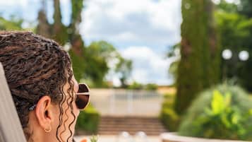 Una persona relajándose junto a una piscina, rodeada de follaje y un cielo despejado.
