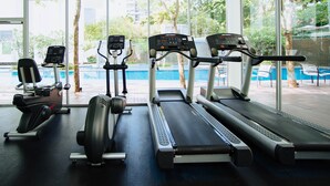 A gym with treadmills, an elliptical, and a rowing machine, overlooking a pool.