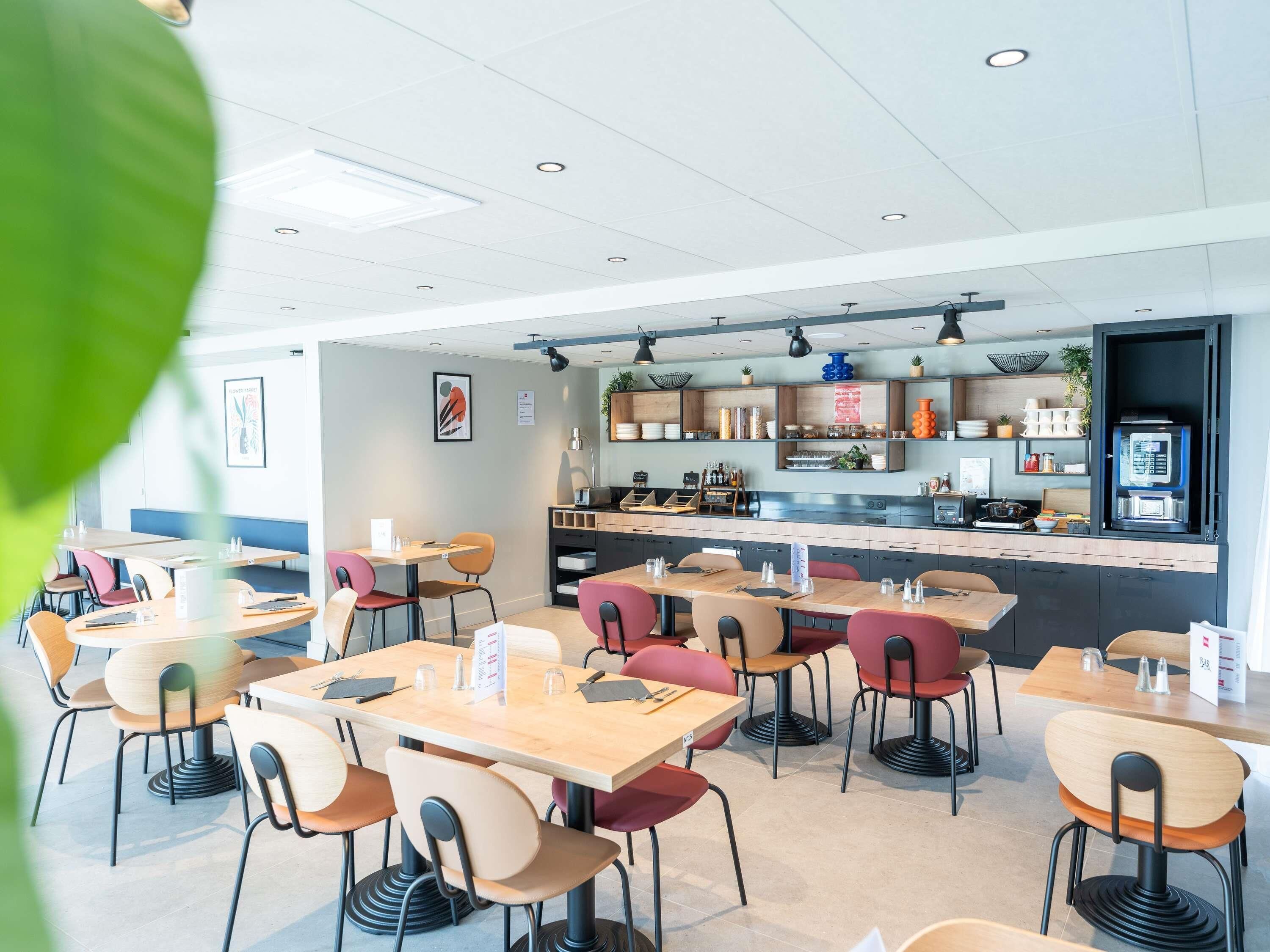 A modern restaurant interior with multiple tables and chairs, a counter with a coffee machine, and shelves with various items.