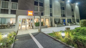 Un hotel moderno con el letrero 'ibis', que presenta una entrada limpia, asientos exteriores y una fachada bien iluminada.