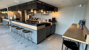 Un área de bar moderna con una barra central, taburetes y una zona de estar con una mesa y sillas.
