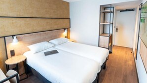 Una habitación de hotel moderna con cama, mesitas de noche, escritorio y estantería empotrada.